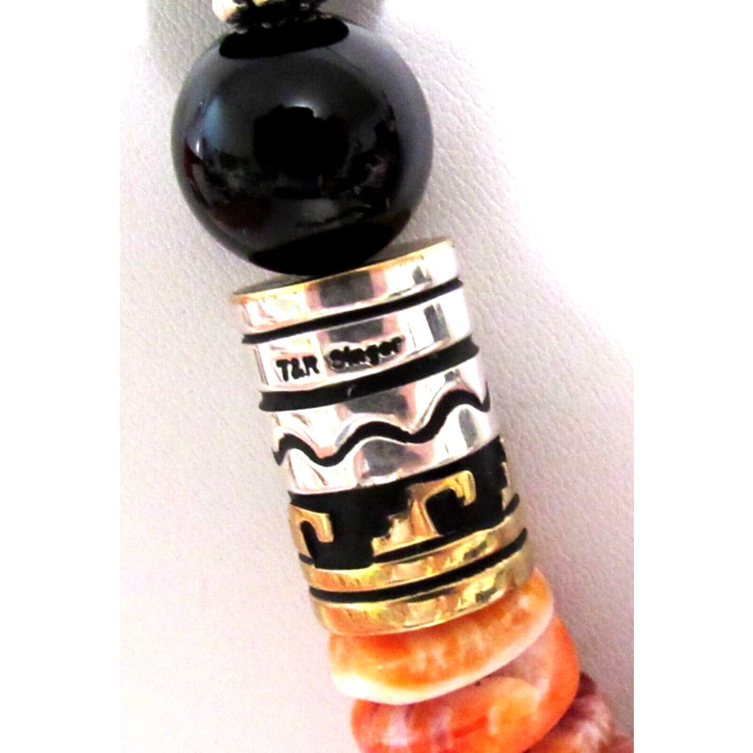 Close-up of Navajo Tommy Singer orange spiny oyster necklace showcasing black beads and intricate silver and gold detailing.
